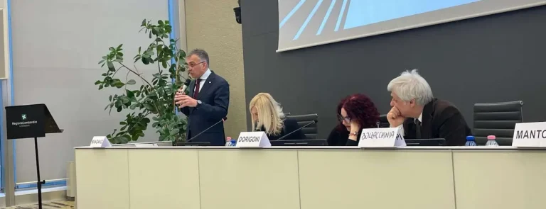 Gregorio Mangano parla al seminario di Milano 2025 e altri relatori seduti lo ascoltano con attenzione