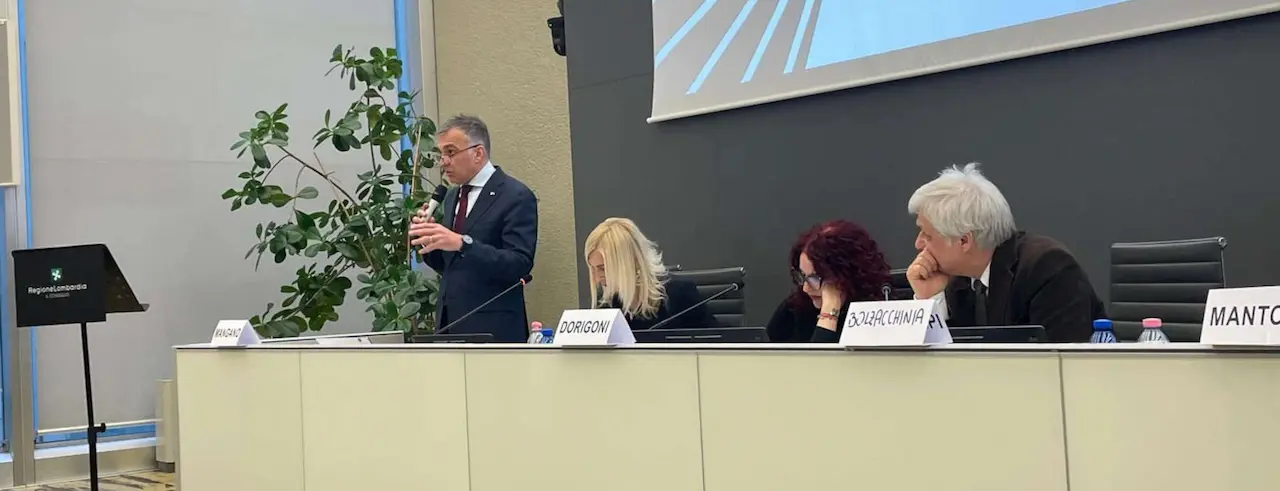 Gregorio Mangano parla al seminario di Milano 2025 e altri relatori seduti lo ascoltano con attenzione