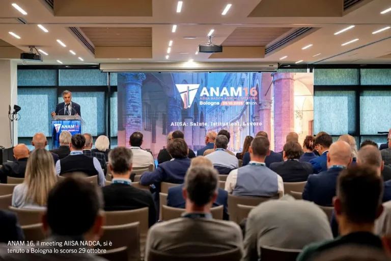 Gregorio Mangano interviene dal podio davanti alla platea durante il meeting ANAM 16 di AIISA NADCA a Bologna, il 29 ottobre 2025. Sullo sfondo, un grande schermo mostra il logo dell'evento.